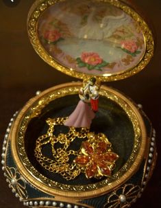 an ornate gold and pink box with a figurine in it's lid