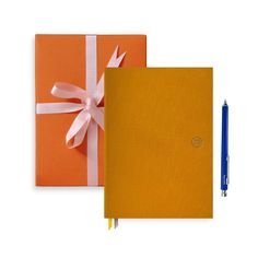 an orange notebook with a white ribbon on it and a blue pen next to it