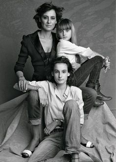 two women and a child sitting on top of a bed in front of a wall