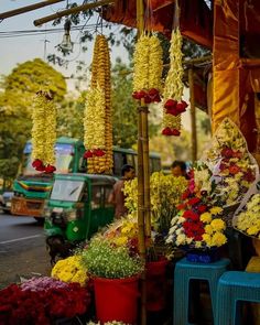 an outdoor market with flowers and plants on the side of the road in front of a green truck