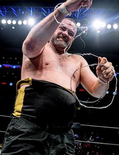 a man with no shirt on standing in the middle of a wrestling ring holding his fist up