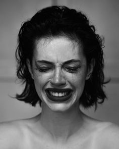 black and white photograph of a woman with her face painted like a clown smiling at the camera