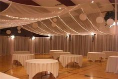 a banquet hall with tables and chairs covered in white tablecloths, lights and drapes