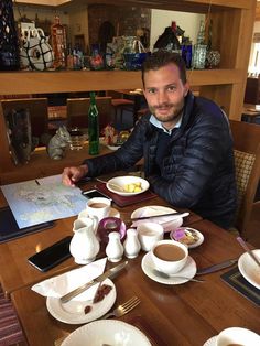 a man sitting at a table with plates and cups on it in front of him