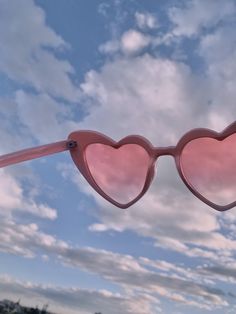 a pair of pink heart shaped sunglasses hanging from the side of a pole with clouds in the background