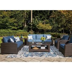 an outdoor patio furniture set with blue cushions and pillows on a rug in front of trees