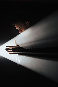 a man standing in the dark with his hands folded out and light coming from behind him