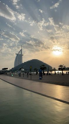 the sun is setting behind a building on the beach with palm trees in front of it