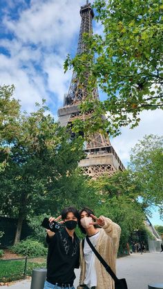 two people taking pictures in front of the eiffel tower