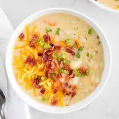 two white bowls filled with soup and topped with bacon, cheese and green onions on a marble surface