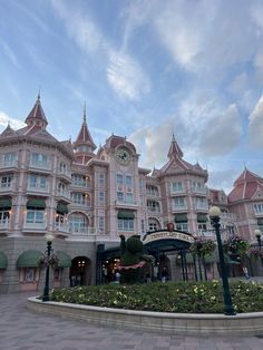 a large pink building with a clock on it's face in front of a flower garden