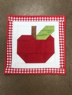 an apple quilted on top of a red and white checkered tablecloth with a green piece in the center