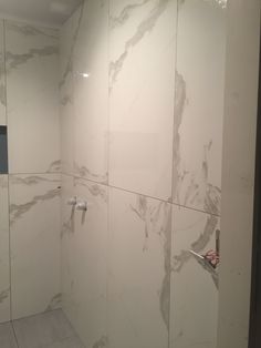 a bathroom with white marble walls and tile flooring, shower head and hand held faucet