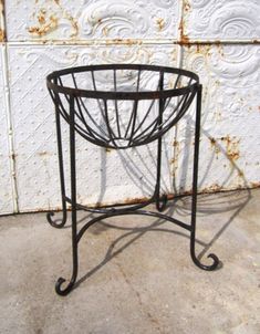 a small metal basket sitting on top of a cement floor next to a white wall