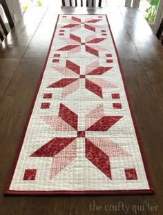 a red and white quilted table runner on top of a wooden floor with chairs