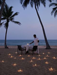 a man standing on top of a sandy beach next to palm trees filled with candles