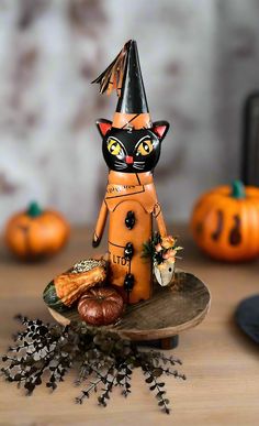 a cat figurine sitting on top of a wooden plate next to pumpkins