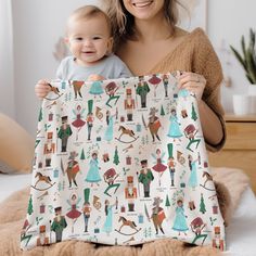 a woman holding a baby in front of a white blanket with cartoon characters on it