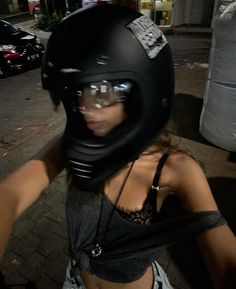 a woman wearing a motorcycle helmet and goggles on the street at night with her hand in her pocket