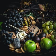 a platter filled with grapes, apples, crackers, cheese and other foods