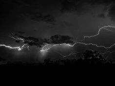 black and white photo of lightning in the sky with trees on either side by itself