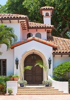 a white house with a brown door and some plants on the front steps in front of it