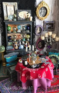 a table with a red cloth on it in front of a shelf filled with pictures and candles