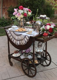 an old fashioned serving cart with flowers and tea cups on the top is filled with pastries