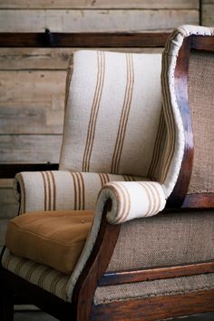 an old chair with a striped seat and back cushion sitting in front of a wooden wall