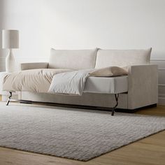 a white couch sitting on top of a wooden floor next to a lamp and rug