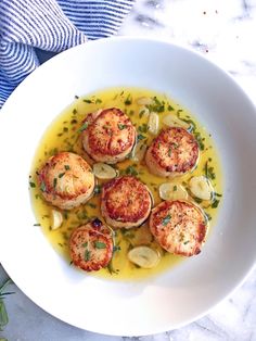 a white plate topped with scallops covered in yellow sauce and garnished with herbs