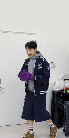 a young boy is standing in front of a door and holding a purple bag while looking at his cell phone