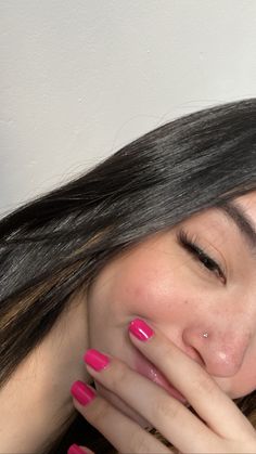 a woman with long black hair and pink nails holding her hand to her face while looking at the camera