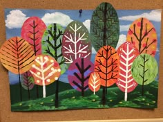 an art project with colorful trees painted on it's paper and hanging from a bulletin board