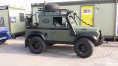 an army green jeep is parked in front of a building with two other vehicles behind it