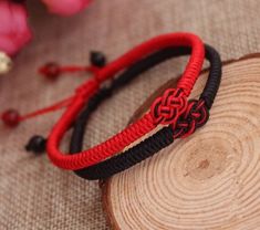 two red and black bracelets sitting on top of a piece of wood next to flowers