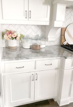 a kitchen with white cabinets and marble counter tops in the center, along with flowers on the stovetop