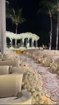 an outdoor wedding setup with white flowers and candles on the ground, surrounded by palm trees