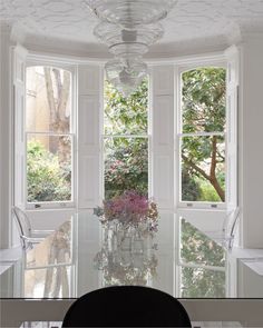 a dining room table with chairs and a vase filled with flowers in front of the window