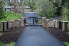 a gated driveway leading to a house with trees in the back ground and bushes on either side