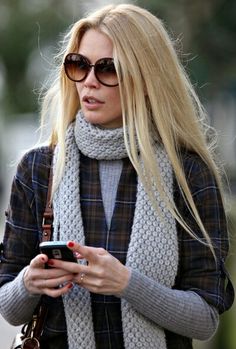 a blonde woman wearing sunglasses and scarf looking at her cell phone while walking down the street