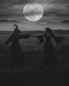 two women in long dresses holding hands with the moon behind them