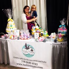 a woman holding a child in front of a table with cakes and cupcakes on it