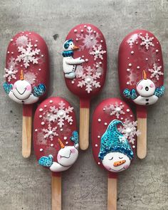 four red popsicles decorated with snowmen and unicorns on wooden skewers