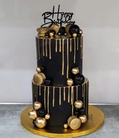 a three tiered black and gold birthday cake with dripping icing on the top