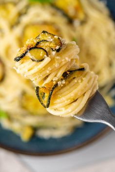 a fork full of pasta with zucchini and spinach on it in a blue bowl