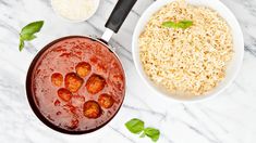 two bowls filled with meatballs and rice on a marble counter top next to basil leaves