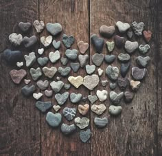 many different rocks arranged in the shape of a heart on a wooden surface, with one being surrounded by smaller ones