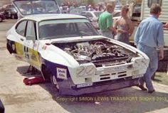 an old race car with the hood open and people looking at it in front of them