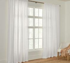 a living room with white curtains and a chair in front of a window that is open